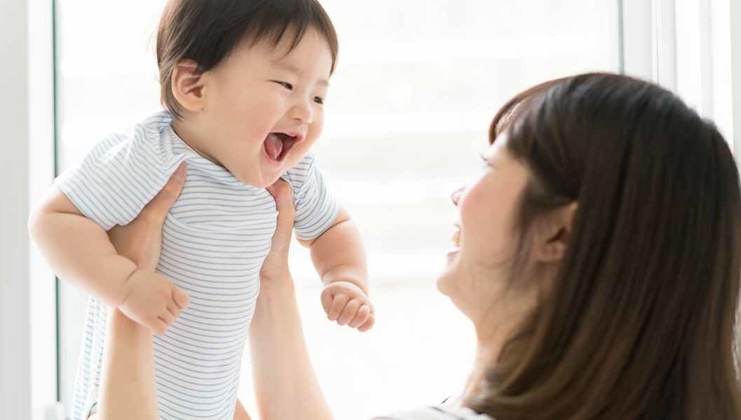 笑顔の赤ちゃんを抱き抱えるママ